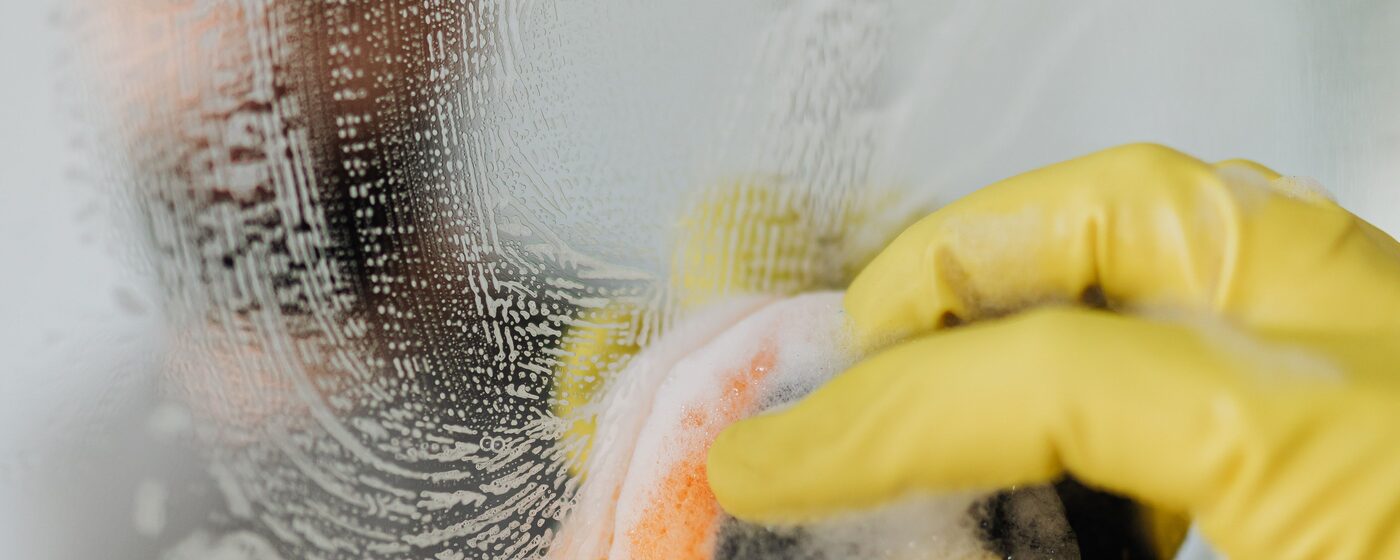 Close-up of a gloved hand scrubbing a glass surface during a deep clean